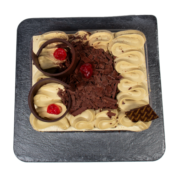 A square cake with chocolate and vanilla swirls, topped with chocolate shavings, chocolate rings, and cherries, viewed from above.