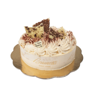 A brunetti tiramisu cake with whipped cream and chocolate shavings on a gold base, partially sliced.
