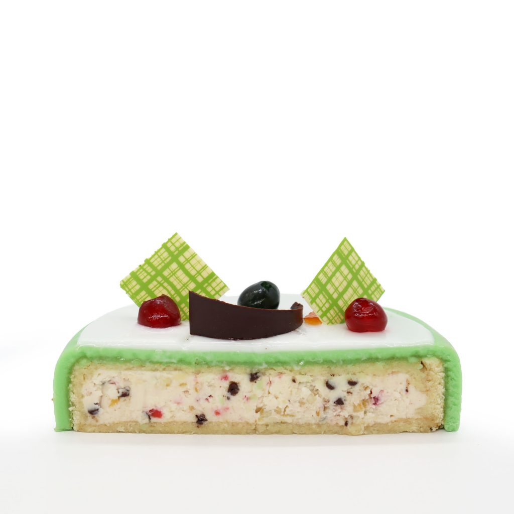 Italian dessert Cassata siciliana. Typical sicilian cheese cake made with  almond, sponge cake, ricotta cheese and candied fruit, cherry and orange,  with shell of green marzipan icing. Dark background. Stock Photo |