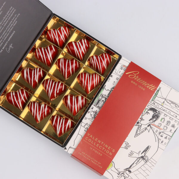 A box of chocolates with red swirl designs, in gold compartments, partly open revealing a chocolatier-themed insert.