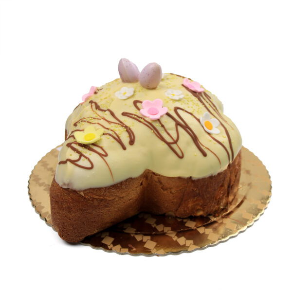 Colomba Con Gelato with yellow icing, decorated with chocolate drizzle, flower-shaped sprinkles, and egg-shaped candies on a gold doily.