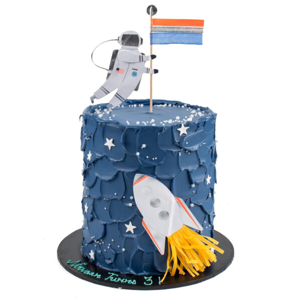 A space-themed cake with a rocket, astronaut, and the flag on top, decorated with stars and craters on a dark blue fondant.