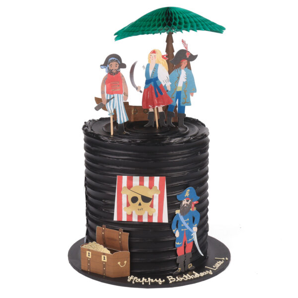 A pirate-themed birthday Black cake with cartoon pirate figures and a treasure chest under a green umbrella, bearing a "happy birthday" inscription.