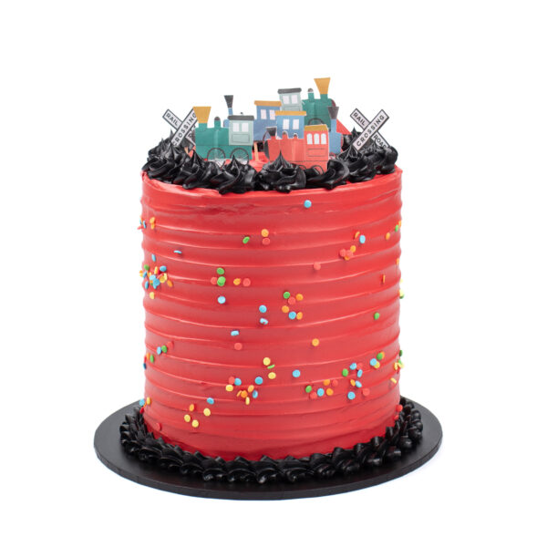 A red frosted cake with multicolored sprinkles and black frosting on top, decorated with a toy train motif.