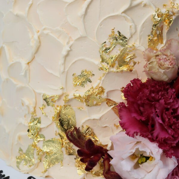 A cake decorated with Gold Leaf and pink flowers.