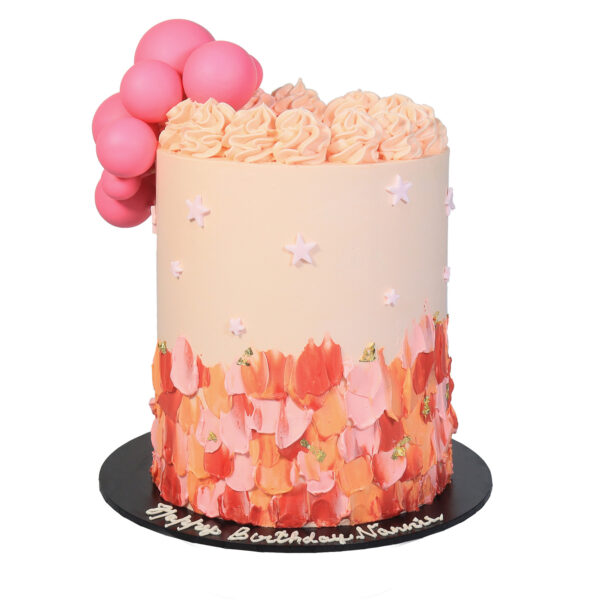 A tall birthday cake with pink frosting and decorative edible flowers, topped with a cluster of pink balloons and the inscription "happy birthday ".