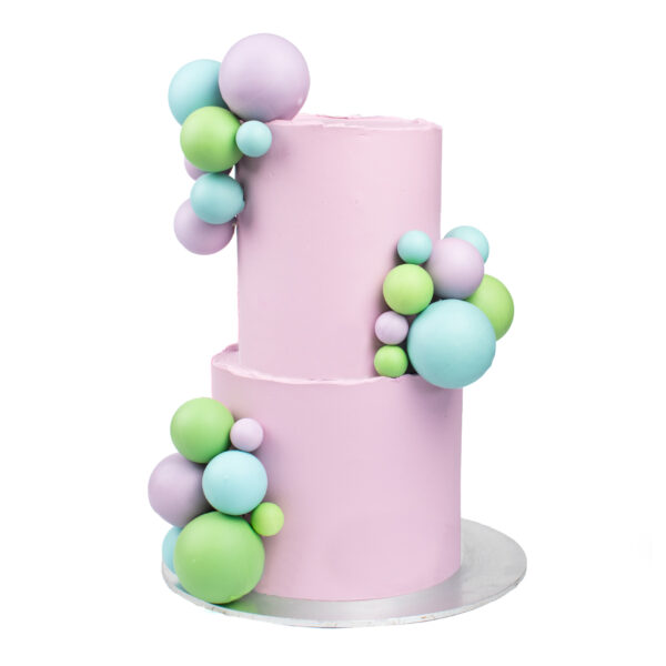 Two-tier pink cake adorned with clusters of pastel blue and green spheres, displayed on a silver base, isolated on a white background.