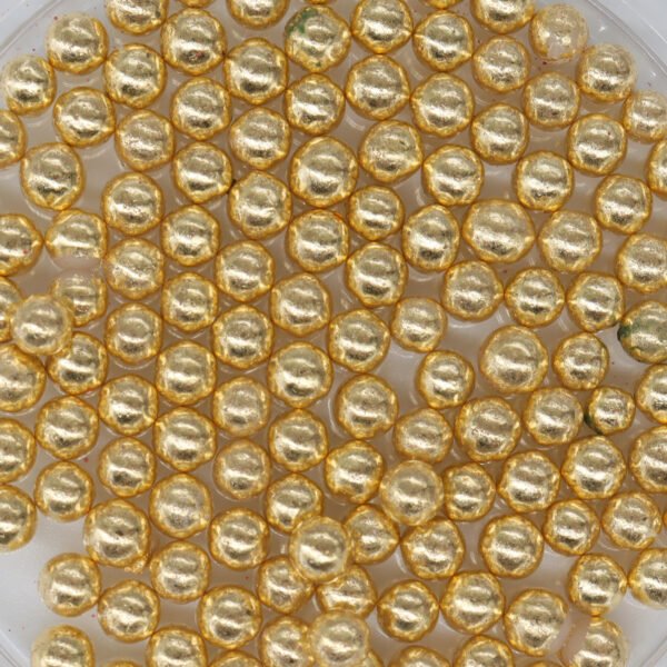 A tray of gold plated beads on a white surface.