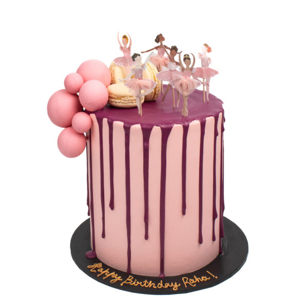 A pink birthday cake adorned with dripping icing, decorative balloons, and ballerina figurines, with "happy birthday Raha!" written on the base.