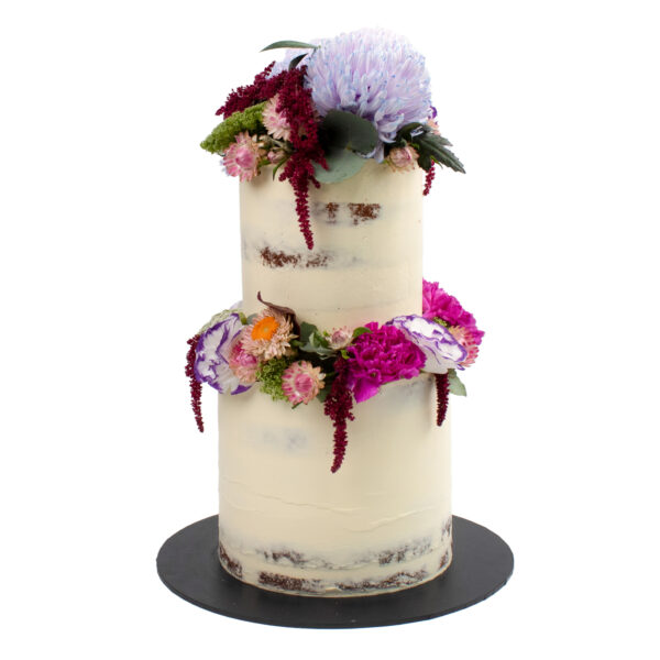 A wedding cake with white icing, decorated with a variety of purple and pink flowers and green leaves, displayed on a black stand.