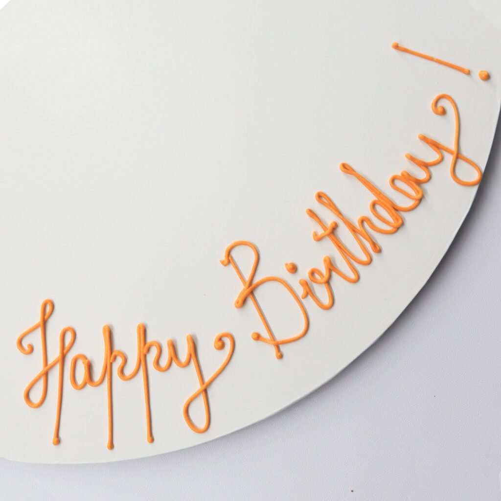 A happy birthday cake with orange lettering on a white plate.