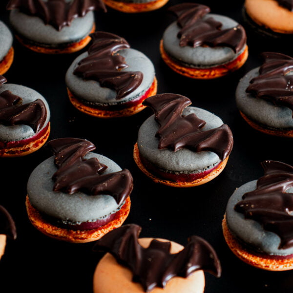 A group of Halloween Macarons - 8 Pack shaped like bats are arranged on a table.