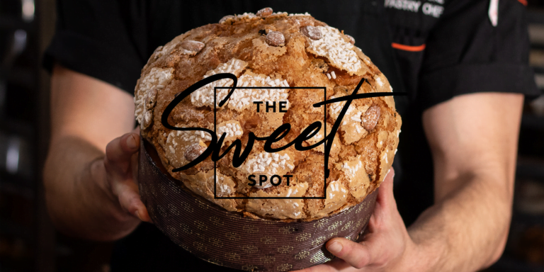 A person holding a large, freshly baked loaf of bread with "the sweet spot" logo across the center.