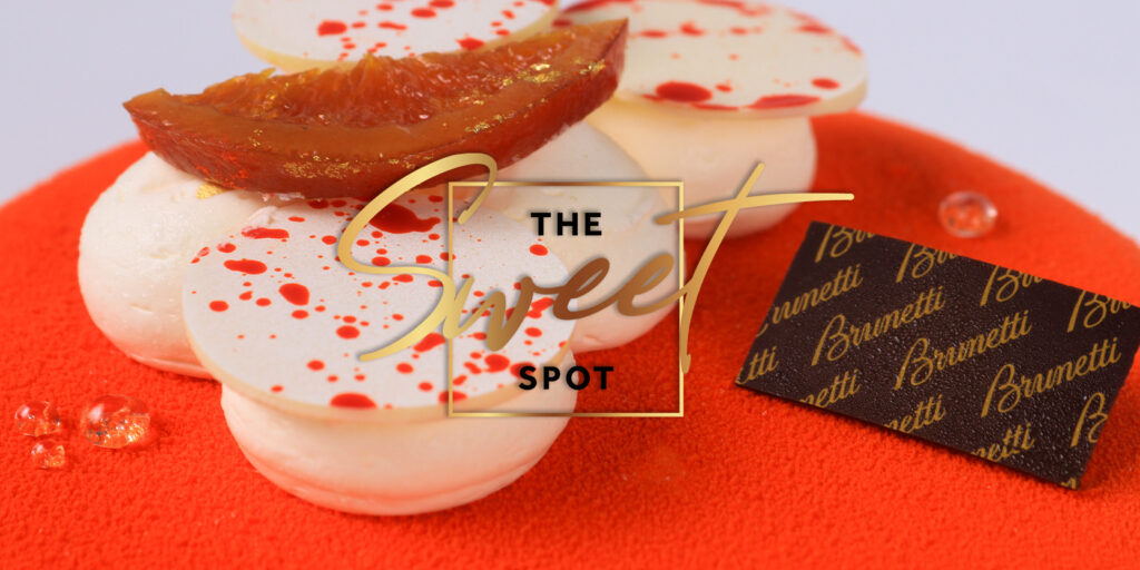 A vibrant orange cake decorated with white icing dollops, and a piece of orange on top with "the sweet spot" text overlay