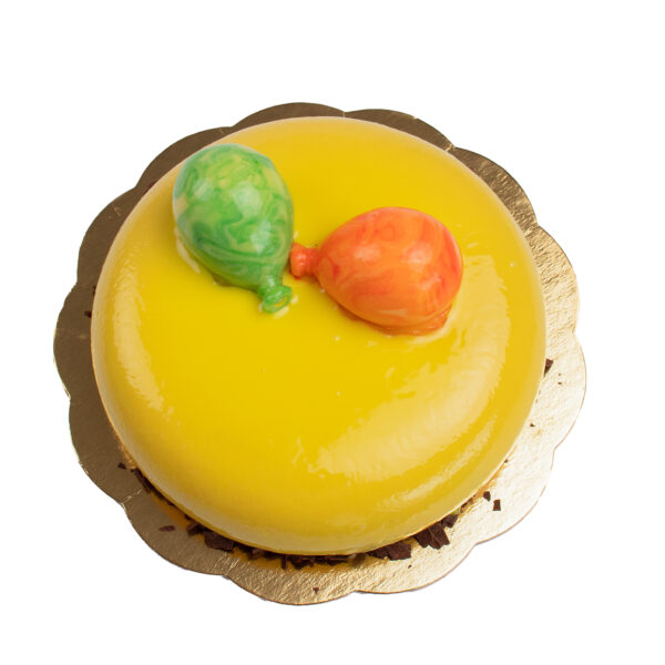 A bright yellow cake topped with two colorful, balloon-shaped candies on a gold cardboard base, isolated on a white background.