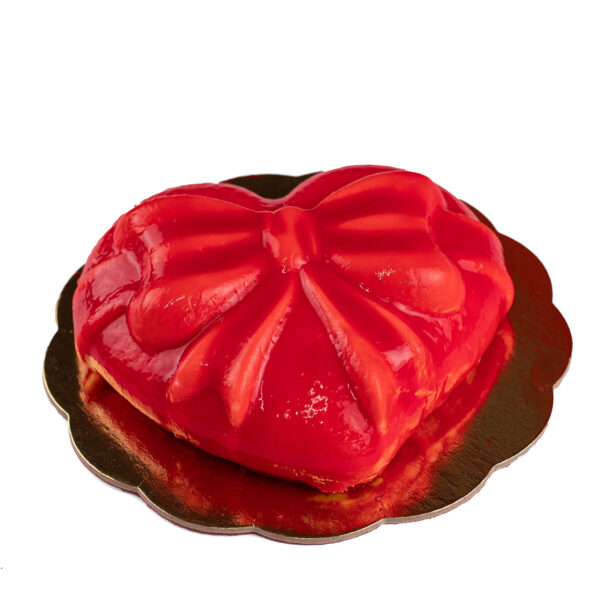 A heart-shaped red gelato cake with a glossy finish on a gold cake board, isolated on a white background.