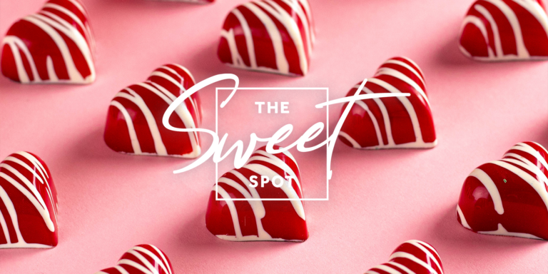 Assorted chocolate candies shaped like hearts with white and red striped patterns, displayed on a pink background with text "the sweet spot".