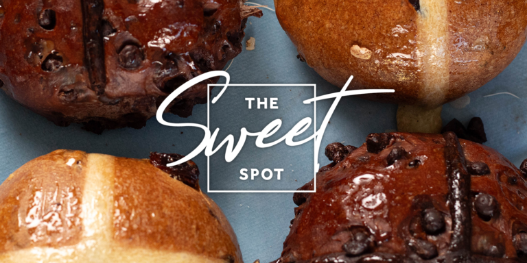 Close-up of freshly baked bread rolls with chocolate chips on a blue surface, with a logo that reads "the sweet spot".