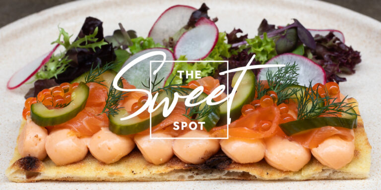 A gourmet flatbread topped with salmon, cream cheese, cucumber, radish, and mixed greens, branded with "the sweet spot" logo in the center.