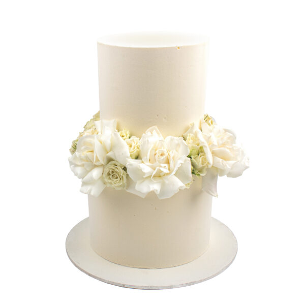 Tall white cake decorated with white and pale yellow roses on a silver base, isolated on a white background.